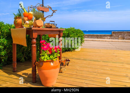 Topf mit Blumen und Restaurant Tisch mit Gemüse auf Holzterrasse dekoriert entlang der Küste in einem kleinen Dorf in der Nähe von Cala Ratjada, Mallorca, Spai Stockfoto