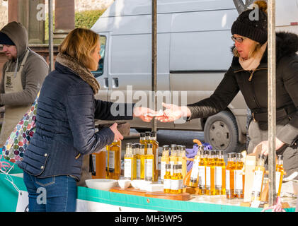 Frau bezahlen in Schwarz & Gold Öle im Freien Markt ausgeht, Haddington Farmers Market, Place d'Aubigny, Court Street, East Lothian, Großbritannien im Winter Tag Stockfoto