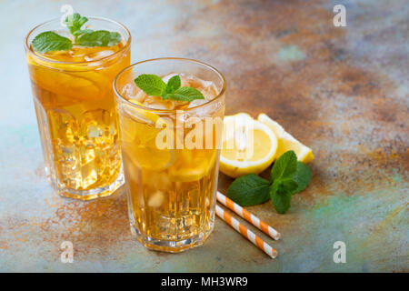 Traditionelle Eistee mit Zitrone, Minze und Eis in hohe Gläser. Zwei Gläser mit kühlen Sommer Drink auf alten rostigen Hintergrund. Stockfoto