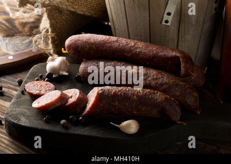 Deutsche Spezialität Salami hart Räucherwurst und mit Gewürzen auf Holzbrett auf Tisch in Scheiben geschnitten Stockfoto