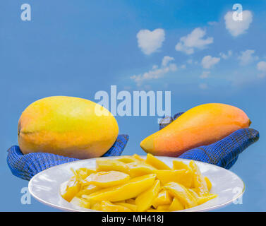 Zusammenfassung das Schneiden von reife Mango Obst auf der Platte die Hand mit dem Handschuh fangen die reife Mango mit dem blauen Himmel Wolke Hintergrund. Stockfoto