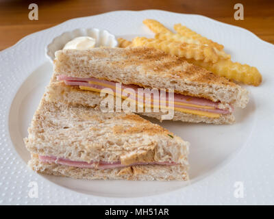 Schinken und Käse Sandwich und Pommes Frites mit Mayonnaise Soße auf weiße Platte auf Holz Tisch im Restaurant. Stockfoto