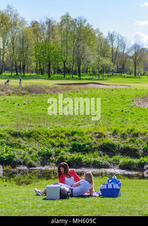 Glasgow, Schottland, Großbritannien. 30. April, 2018. UK Wetter: Zwei Mädchen sitzen auf dem Gras am Ufer der Weißen Warenkorb Wasser mit Pollok Golfkurs im Hintergrund auf einem warmen und sonnigen Tag im Pollok Country Park. Credit: Skully/Alamy leben Nachrichten Stockfoto