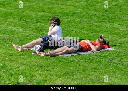 Glasgow, Schottland, Großbritannien. 30. April, 2018. UK Wetter: Zwei Sonnenanbeter, die auf dem Gras am Ufer der Weißen Warenkorb Wasser an einem warmen und sonnigen Tag im Pollok Country Park. Credit: Skully/Alamy leben Nachrichten Stockfoto