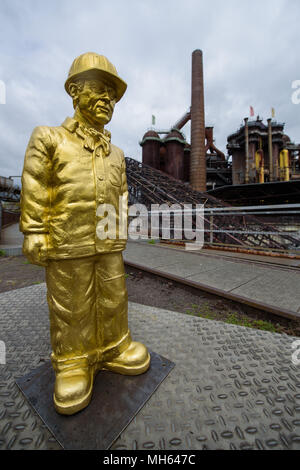 30 April 2018, Deutschland, Völklingen: Die Figur der ein Beschäftigter im Laufe der Skulptur Projekt Second Life - 100 Arbeitnehmer von Ottmar Hoerl im Weltkulturerbe Völklinger Hütte. 100 kleine rot, gold und grau Zahlen sind auf dem Gelände der ehemaligen Schmiedearbeiten ausbreiten. Foto: Oliver Dietze/dpa Stockfoto