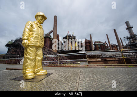 30 April 2018, Deutschland, Völklingen: Die Figur der ein Beschäftigter im Laufe der Skulptur Projekt Second Life - 100 Arbeitnehmer von Ottmar Hoerl im Weltkulturerbe Völklinger Hütte. 100 kleine rot, gold und grau Zahlen sind auf dem Gelände der ehemaligen Schmiedearbeiten ausbreiten. Foto: Oliver Dietze/dpa Stockfoto