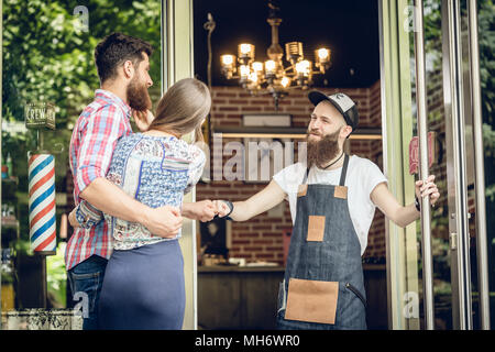 Cool hairstylist mit einer Faust bump zu einem glücklichen Kunden an der Tür eines Salon Stockfoto