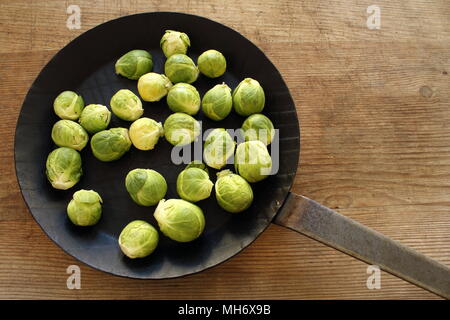 Zusammensetzung von frischem Rosenkohl eine eiserne Pfanne auf einem Holzbrett Stockfoto