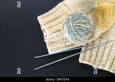 Eine Kugel aus Wolle mit Stricknadeln und Socken auf einem grauen Tabelle. Handarbeit Stockfoto