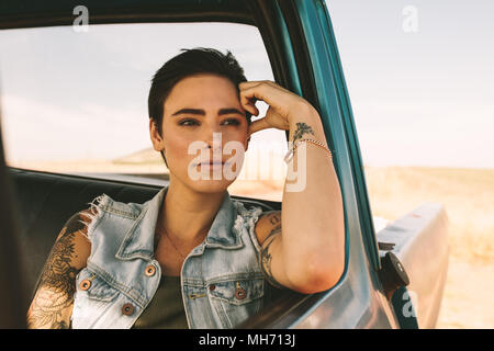 Frau auf einer Reise in einem Auto. Frau mit Tattoos auf Arme, die aus ihrem Auto am Fenster sitzen. Stockfoto