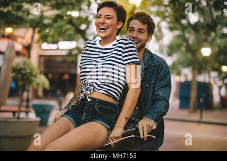 Glückliches Paar gehen für eine Radtour. Frau sitzt auf Freunde Fahrradlenker und Lachen. Stockfoto