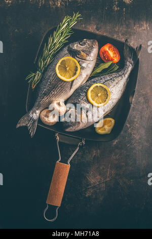 Blick von oben auf die Fisch mit Gemüse und Gewürze in Backform auf unebenem Untergrund. Stockfoto