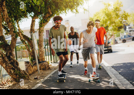 Zwei Männer Schlittschuhlaufen auf Skateboard auf einem Gehsteig, während ihre Gehilfen feuern Sie. Basketball Jungs gehen auf Asphalt mit skateboards. Stockfoto