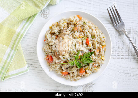 Blick von oben auf eine köstliche, hausgemachte, traditionelle bulgarische Hühnereintopf mit Reis und Gemüse in weiße Platte auf einem rustikalen Holztisch. Stockfoto