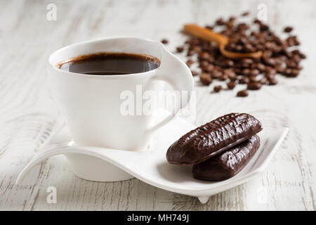 Kaffee am Morgen in weiße Keramiktasse mit Wave geformten Untertasse und zwei Kakao Kekse auf weißen Holzmöbeln rustikal Tisch Stockfoto