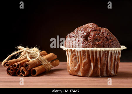 Nahaufnahme eines köstlichen Schokolade Muffin mit Zimtstangen auf einem Holztisch auf schwarzem Hintergrund. Platz für Text Stockfoto
