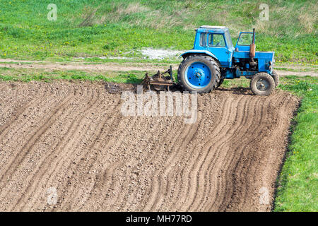 Blue dusty Traktor mit saatbeet Kultivator stehen am Rande des frisch gepflügt und bebautes Feld, den Boden für die Aussaat vorbereitet. Landwirtschaft, Landwirtschaftliche Stockfoto