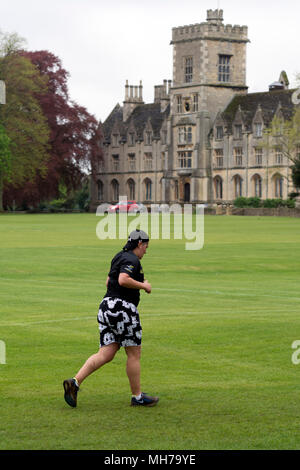 Ein Läufer in Cirencester parkrun mit der Königlichen Universität für Landwirtschaft in der Ferne, Gloucestershire, VEREINIGTES KÖNIGREICH Stockfoto