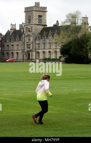 Ein Läufer in Cirencester parkrun mit der Königlichen Universität für Landwirtschaft in der Ferne, Gloucestershire, VEREINIGTES KÖNIGREICH Stockfoto