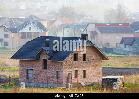 Marke neue geräumige brick Zweistöckiges Wohnhaus mit Fliesen Dach und Fenster Öffnungen in Suburban Nachbarschaft auf dem Hintergrund der fernen Stadt. Buil Stockfoto