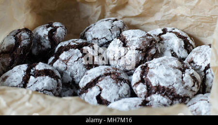 Schokolade crinkle Plätzchen mit Puderzucker Puderzucker. Gebrochene Schokolade Kekse auf dem Papier Hintergrund. Bis zu schließen. Seitenansicht Stockfoto