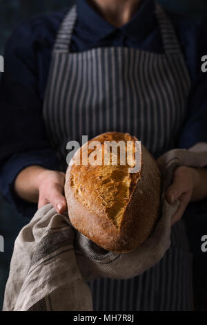 Baker Holding frisches hausgemachtes Brot. Zusammensetzung in dunklen Farben Stockfoto