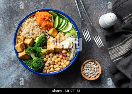 Bunte Buddha Schüssel auf dunklem Hintergrund, Ansicht von oben. Buddha Schüssel mit Quinoa, Tofu, Brokkoli, süsse Kartoffeln, Kichererbsen und Gurke. Gesunde vegetarische sa Stockfoto