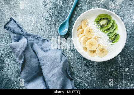 Joghurt mit Banane, Kiwi, Kokos Schüssel. Vegan Joghurt mit Früchten. Gesunde Ernährung, Diät, Fitness, gesunde Lebensweise Konzept. Tabelle Ansicht von oben Stockfoto