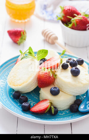 Mini Käsekuchen mit Früchten auf einem blauen Schild. Kalten Sommer Dessert oder Snack. Gesunde Cottage Käse Käsekuchen mit Beeren und Früchte Stockfoto