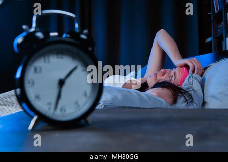 Bild der Frau mit Schlaflosigkeit mit Rosa Auge verband liegend auf Bett neben Wecker Stockfoto