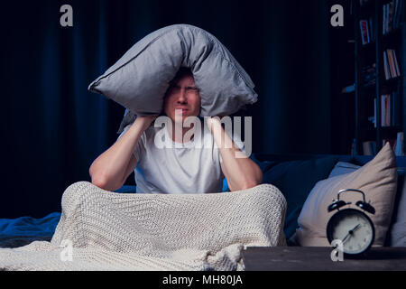 Foto von Mann mit Schlaflosigkeit mit Kissen auf dem Kopf Stockfoto