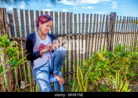 Eine asiatische Frau sitzt gegen einen Zaun an einem Beach Resort das Senden und Empfangen von E-Mails auf Ihrem iPad auf Palawan, Philippinen. Stockfoto