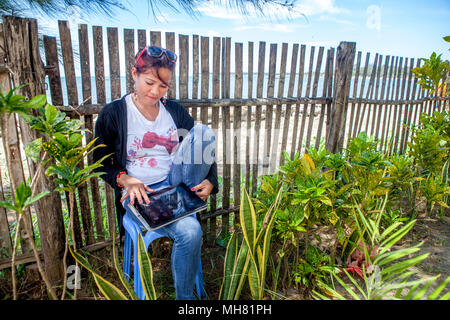 Ein Filipino Frau sitzt auf einem Stuhl an einem Beach Resort auf der Insel Palawan auf den Philippinen, in Kontakt zu bleiben mit Ihrer Familie und Freunden über ihren iPad. Ich Stockfoto