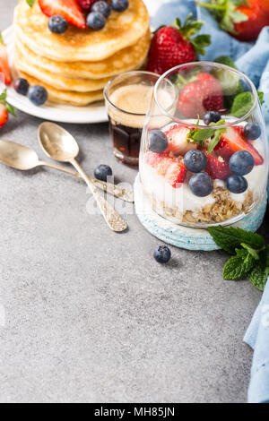 Gesundes Frühstück mit Haferflocken Müsli mit Beeren und Joghurt und panccakes auf Hellgrau konkreten Hintergrund. Gesunde Ernährung Konzept mit kopieren. Stockfoto