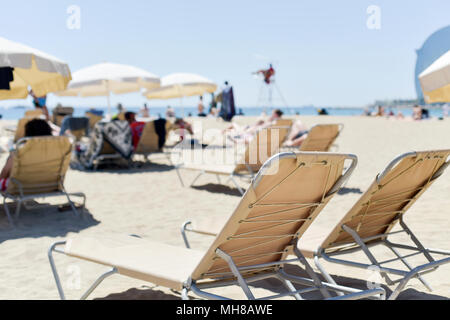 Nahaufnahme von einigen beige liegen und einige beige Sonnenschirme in La Barceloneta Beach, in Barcelona, Spanien, mit unkenntlich Menschen Sonnenbad in der Stockfoto