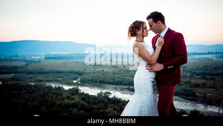 Sensible Hochzeit Portrait der niedlichen jungvermählte Paar. Hintergrund der herrlichen Landschaft bei Sonnenuntergang. Stockfoto