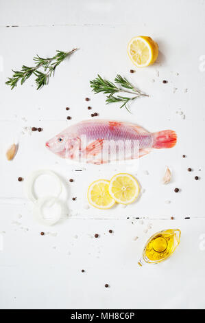Frische Tilapia auf weißem Holz- strukturierten Hintergrund mit frischem Rosmarin und Zitrone. Kulinarische mediterrane Fischgerichte. Stockfoto