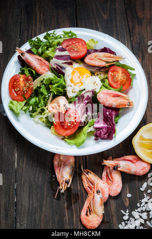 Gesunde Garnelen und Rucola Salat mit Tomaten auf einem Holztisch. Stockfoto