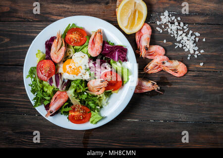 Gesunde Garnelen und Rucola Salat mit Tomaten auf einem Holztisch. Stockfoto