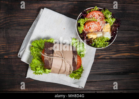 Sandwich auf dem Holztisch mit Schichten von frischen Tomaten, Schinken, Käse und Salat. Stockfoto