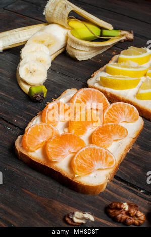 Sandwiches mit Banane, Mandarine, Marmelade, Zitrone, Brot auf Holz Hintergrund. Leckere kalte Snacks. Vegetarische Gerichte. Stockfoto