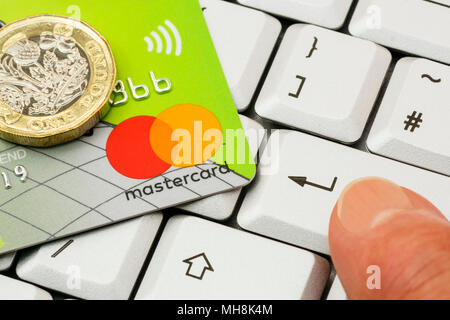 Lloyds Bank Mastercard Kontaktlose Kreditkarte und Einpfundstück auf einer Tastatur mit dem Finger einer Person Drücken der ENTER-Taste. Online shopping Konzept. Großbritannien Stockfoto