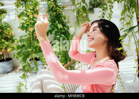 Schöne asiatische junge Frau entspannend und mit Handy auf dem Balkon zu Hause Stockfoto