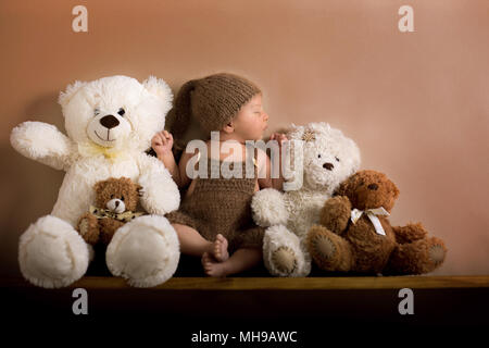 Neugeborenes Baby Boy trug einen braunen Hut und Hosen aus Gewirken tragen, schlafen auf einem Regal neben Teddybären. Im Studio auf einem cremigen Hintergrund Geschossen, geschossen Stockfoto