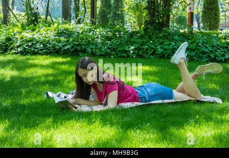 Junges Mädchen mit einem Buch in einem malerischen Park, sonnigen Tag. Das Mädchen der asiatischen Aussehen Stockfoto
