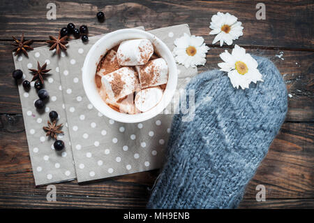 Gestrickte Handschuhe und heiße Schokolade in weißen Herzen Schale mit Marshmallow und Zimt, Nahaufnahme Stockfoto
