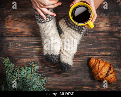 Beine der Mädchen in warme Wollsocken und eine Tasse Kaffee wärmen, winter Morgen zu Hause. Stockfoto