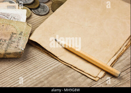 Alte Banknoten und Münzen und Bleistift auf einem Holztisch Stockfoto