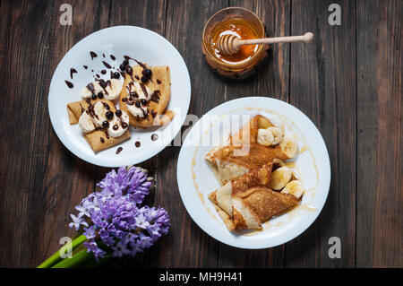 Pfannkuchen mit Schokolade, Honig und Banane auf einem hölzernen Hintergrund. Stockfoto