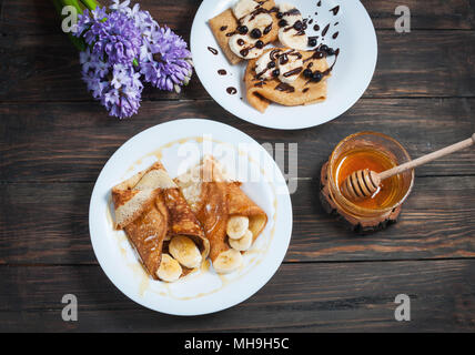 Pfannkuchen mit Schokolade, Honig und Banane auf einem hölzernen Hintergrund. Stockfoto